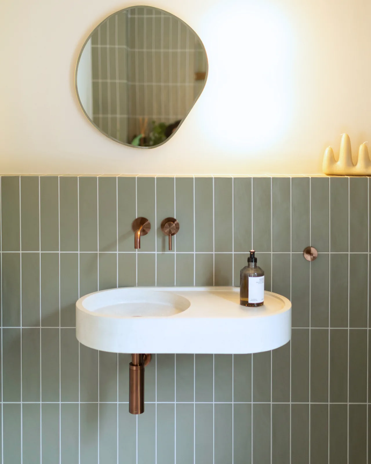 Daphne basin in white concrete under sage green tiles, with copper wall taps