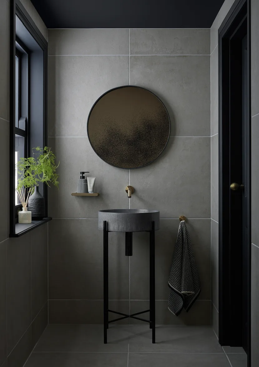 Charcoal Omoi basin on a black stand in a grey tiled cloakroom