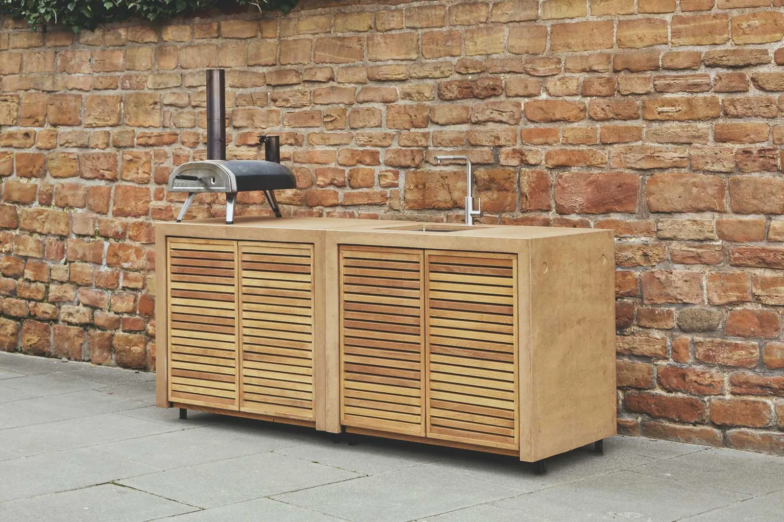 An iroko MOK outdoor kitchen run against a brick garden wall
